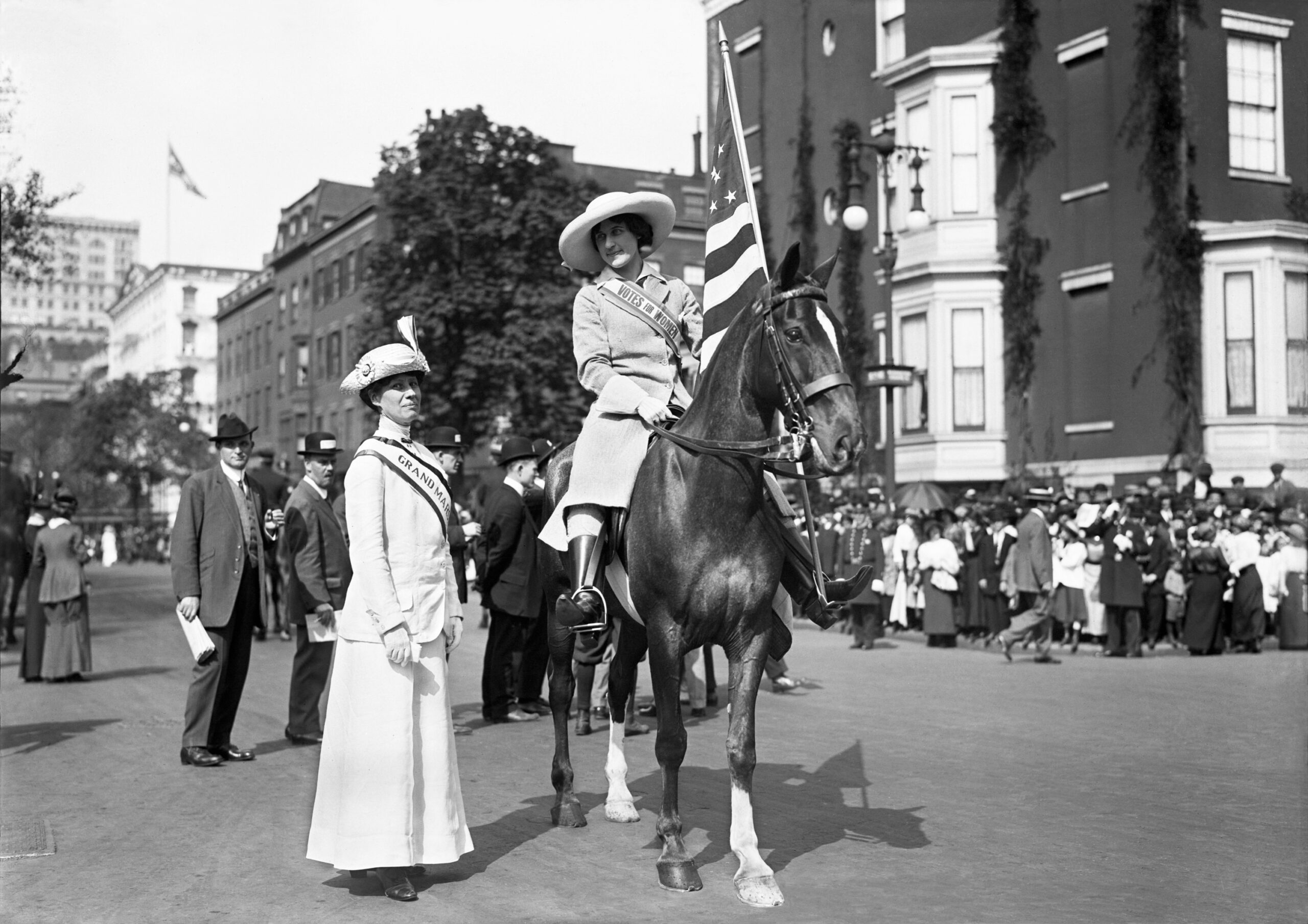 Misses Beiderhase and Milholland, 1912. Shot in New York City, May 4, 1912. Image of two women suffragists wearing banners. The woman on the left standing, is Josephine Beiderhase. The woman on the right seated on a horse carrying an American flag is Inez Milholland. (Mystic Seaport Rosenfeld Collection ANN.1984.187.6818)